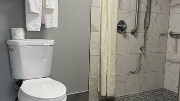 A bathroom with a toilet, a shower with a grab bar, and a towel rack with folded towels.