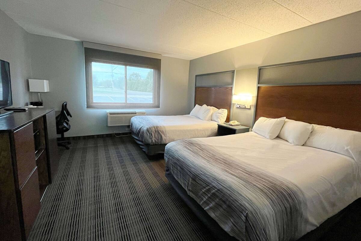 A hotel room with two beds, a desk with a chair, a TV, and a window.