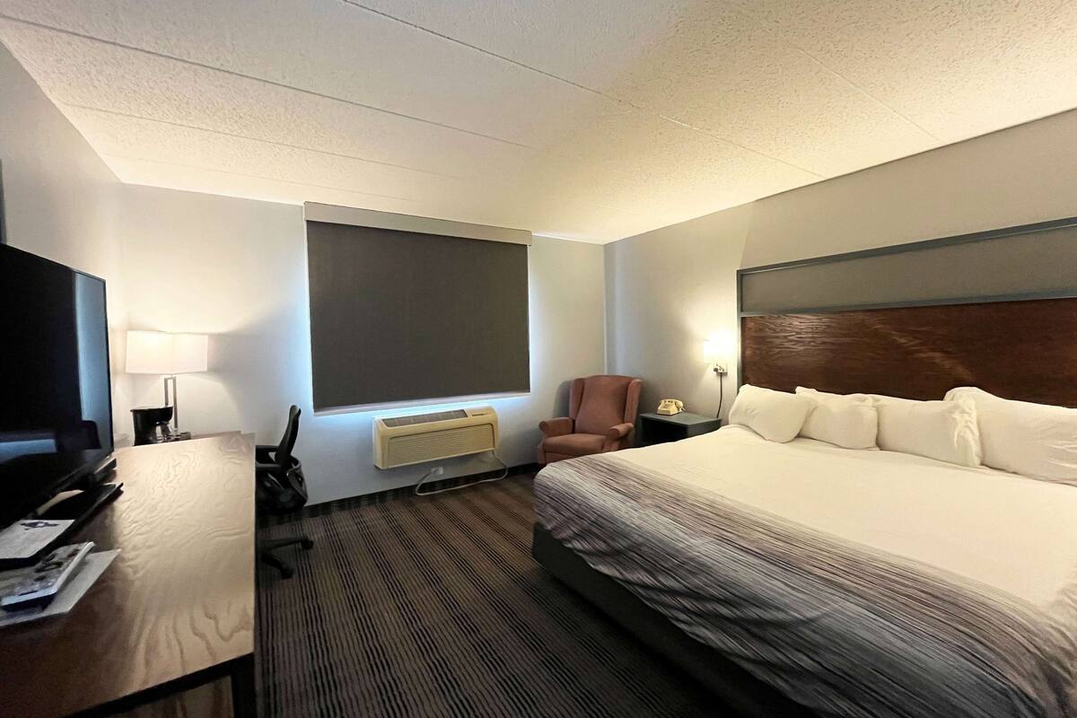 A hotel room with a large bed, a desk with a computer, a chair, a TV, and a window.