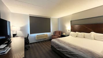 A hotel room with a large bed, a desk with a computer, a chair, a TV, and a window.