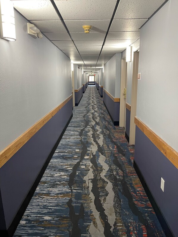 A long, narrow hotel corridor with patterned carpet, light blue walls, and wooden trim.