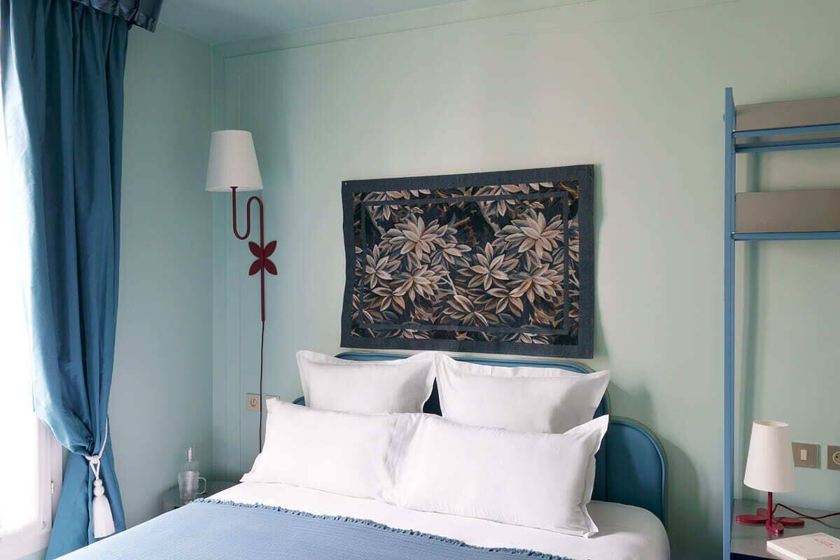 A hotel room with a bed, a nightstand, a lamp, and a wall art piece.