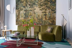 A living room with a green sofa, a glass coffee table, and a large painting of a forest. - Hôtel Beauregard  (Paris)