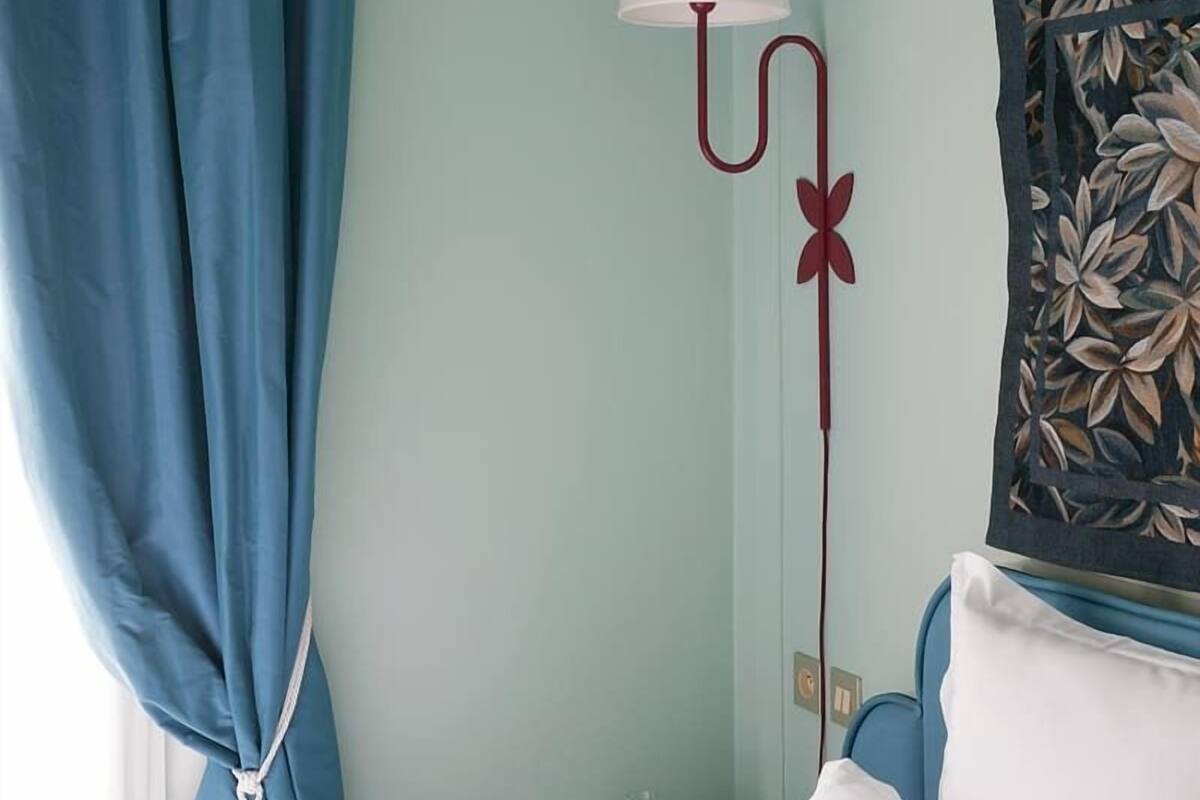A hotel room with a bed, a nightstand, a lamp, and a wall with a floral artwork.