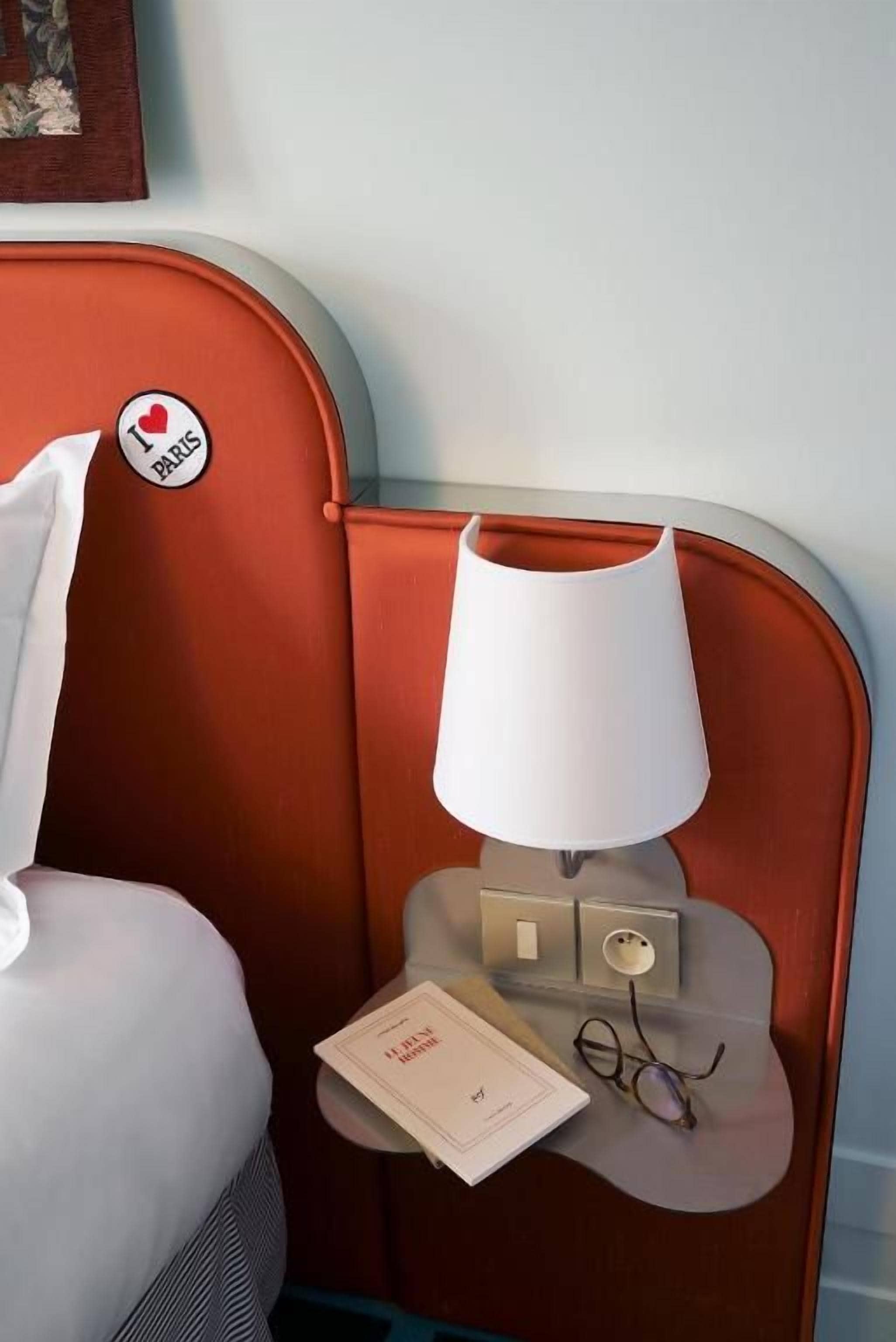 Ein Hotelzimmer mit einem Bett, einem Nachttisch mit Lampe, einem Buch und einer Brille.