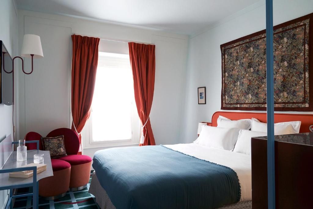 Una habitación de hotel con cama, escritorio con silla, sofá rojo y un cuadro grande en la pared.