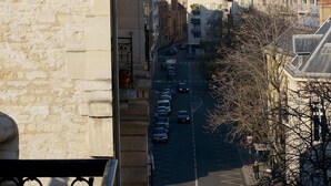 Straßenansicht mit dem Eiffelturm im Hintergrund, Steinbauten und geparkten Autos.