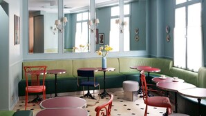 Ein Zimmer mit einem grünen Sofa, roten Stühlen und mehreren kleinen Tischen.