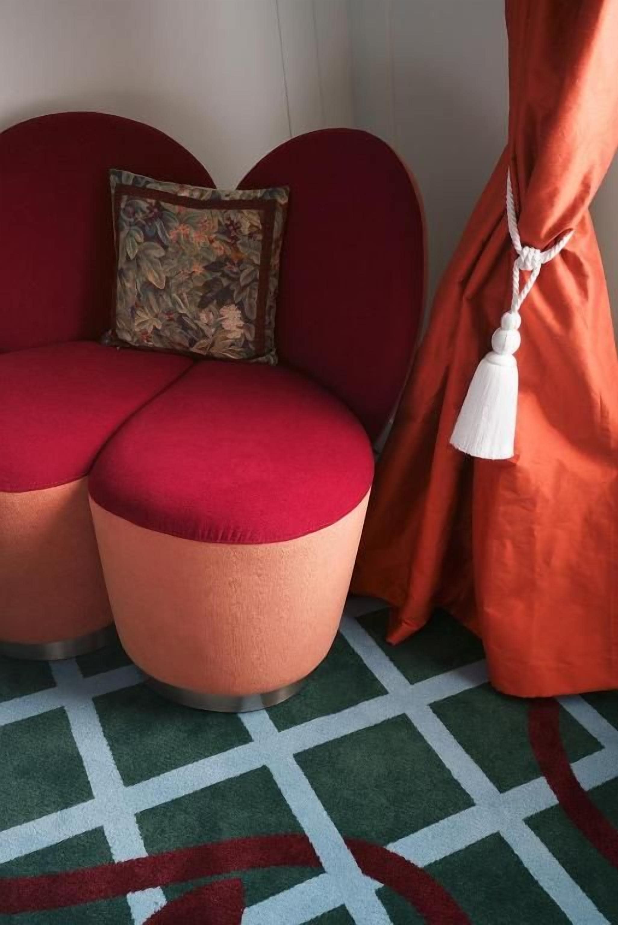 Zona d'estar amb dos poufs rodons, un coixí estampat i una borla blanca penjant d'una cortina.
