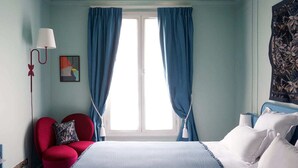 Ein Schlafzimmer mit einem Bett, einem roten Sessel, einem Nachttisch, einer Lampe und einem Fenster mit blauen Vorhängen.