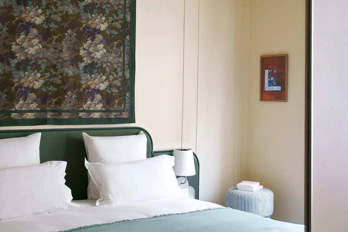 A hotel room with a bed, a green headboard, a floral artwork, a framed picture, and a radiator.