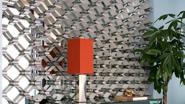 Ein modernes Interieur mit geometrischem Wanddesign, einem spiegelnden Schrank und einem Blumentopf.