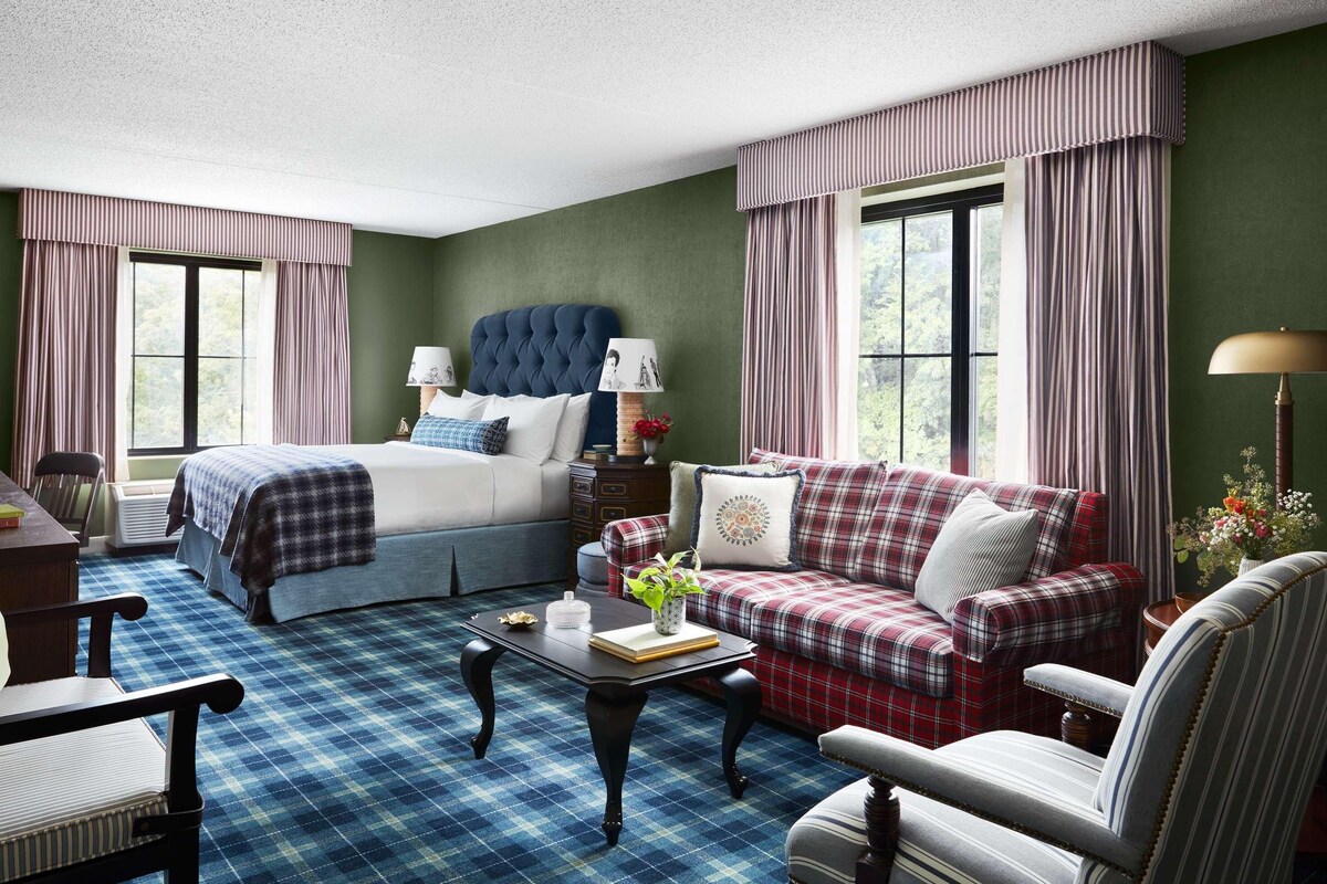 A room with a bed, a sofa, a chair, a table, and a window with curtains.