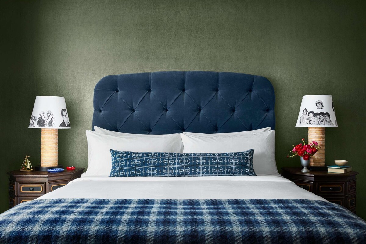 A bed with a tufted headboard, white and patterned pillows, a plaid blanket, and two bedside tables with lamps and decorative items.