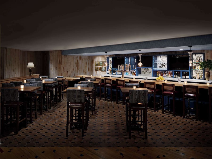 A bar area with wooden paneling, a counter with bottles, and seating with patterned cushions.