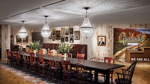 A dining area with a long table, red chairs, chandeliers, framed pictures, and a poster on the wall. - Graduate by Hilton Storrs (Storrs)