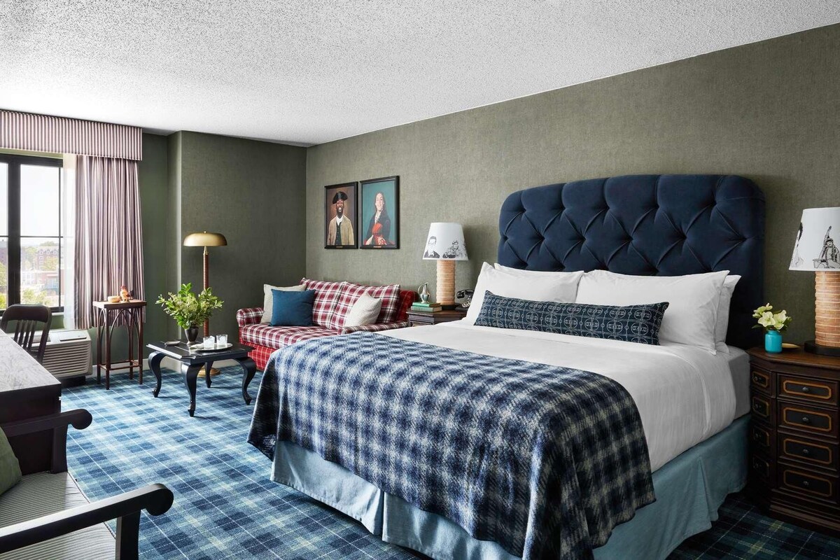 A hotel room with a large bed, a desk, a chair, a sofa, and a window with curtains.