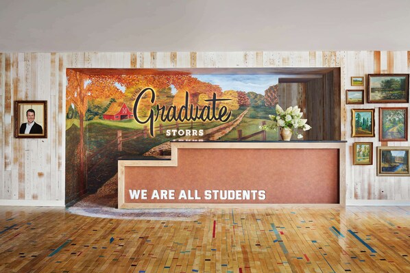 A reception desk with a mural of a rural landscape and the text "Graduate Storrs" and "We are all students".