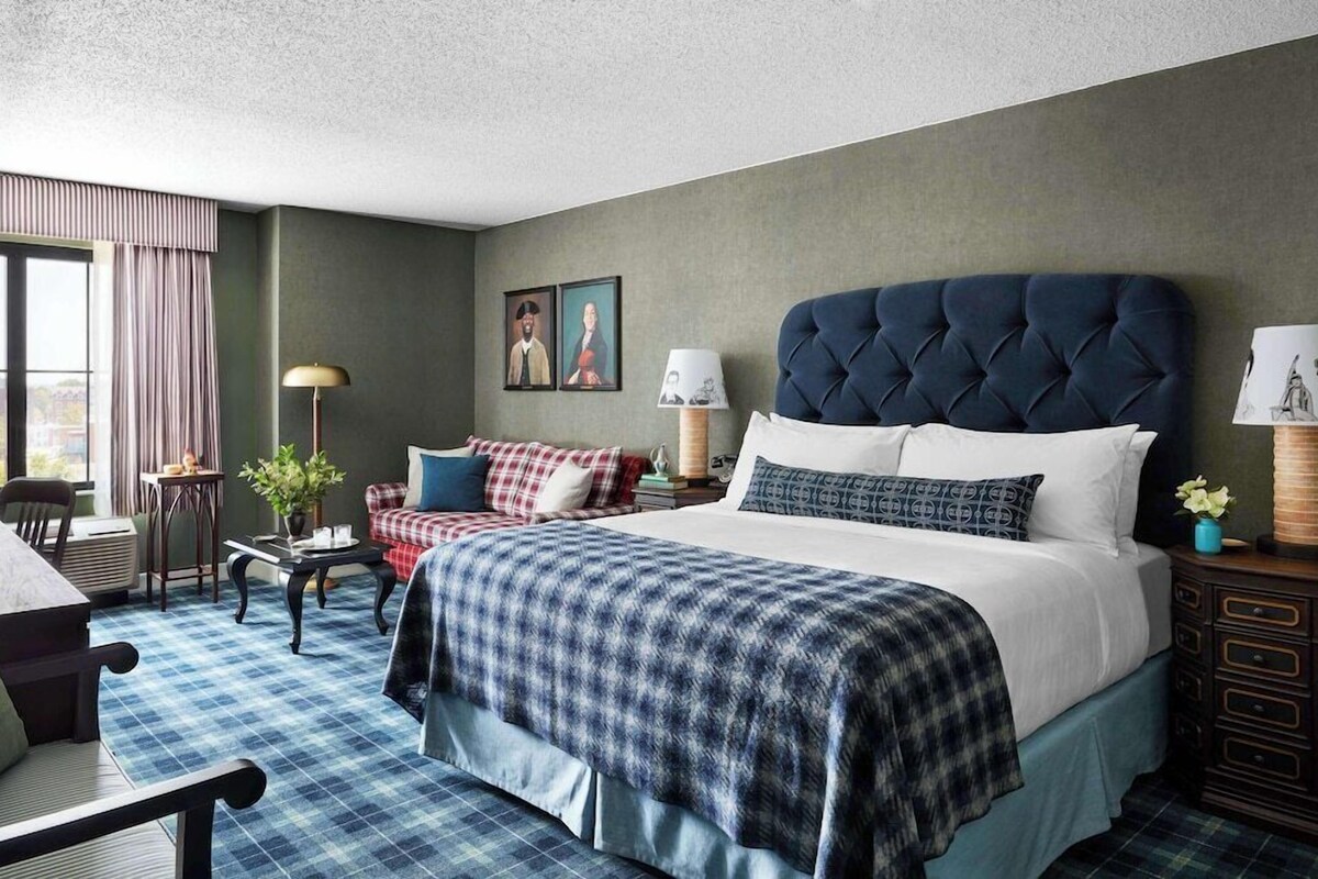 A hotel room with a large bed, a sofa, a desk, and a window with curtains.