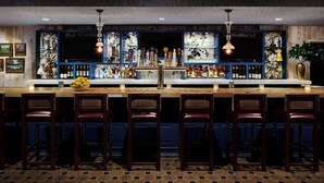 A bar with a long counter, multiple bar stools, and a variety of bottles and glasses. - Graduate by Hilton Storrs (Storrs)