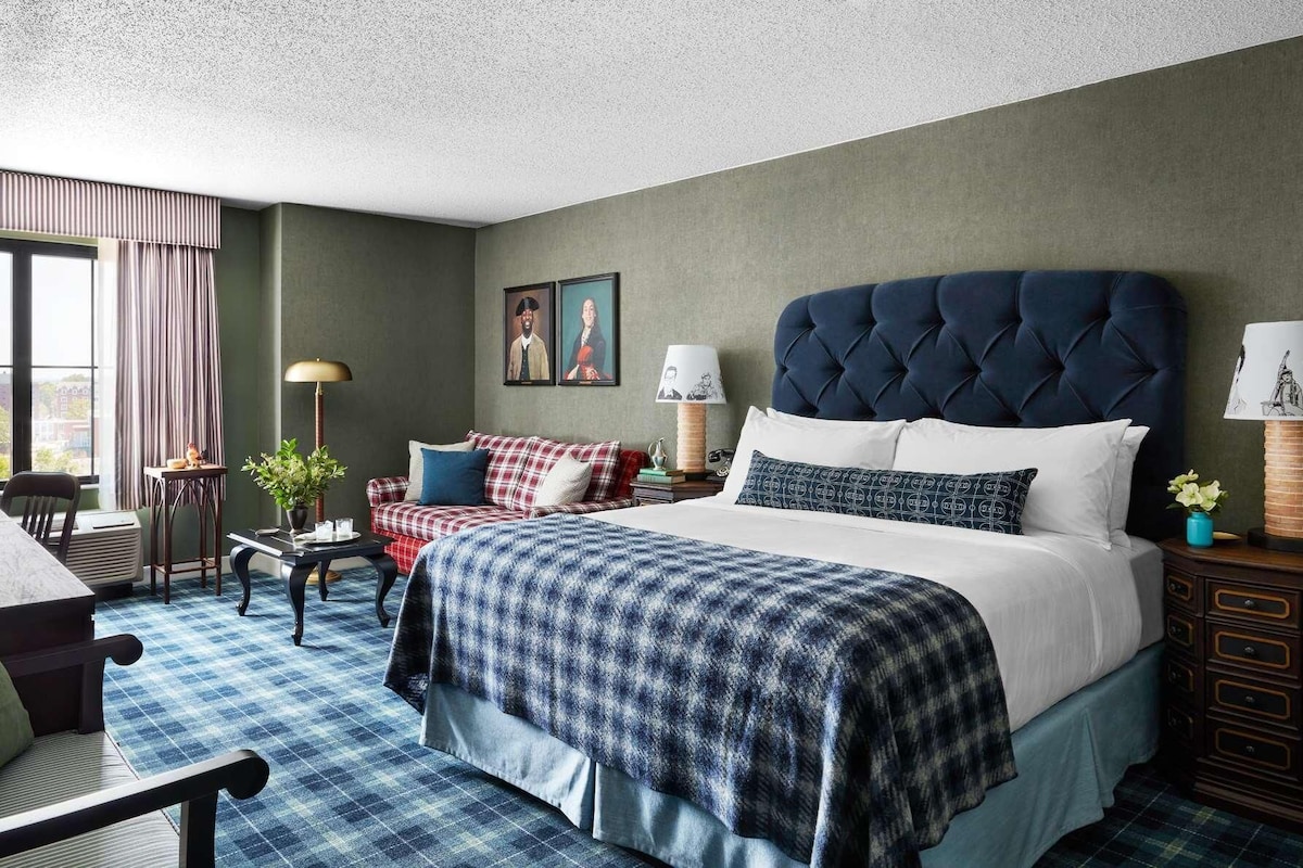 A hotel room with a large bed, a desk, a chair, a sofa, and a window with curtains.