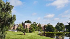 A well-maintained lawn with a pond, surrounded by trees and a building with a red brick facade. - Graduate by Hilton Storrs (Storrs)