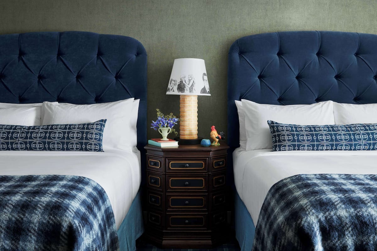 A double bed with a tufted headboard, a bedside table with a lamp, and a decorative rooster figurine.