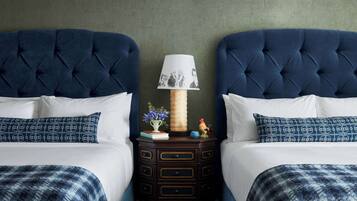 Una cama doble con cabecera capitonada, una mesita de noche con lámpara y una figurita decorativa de gallo.