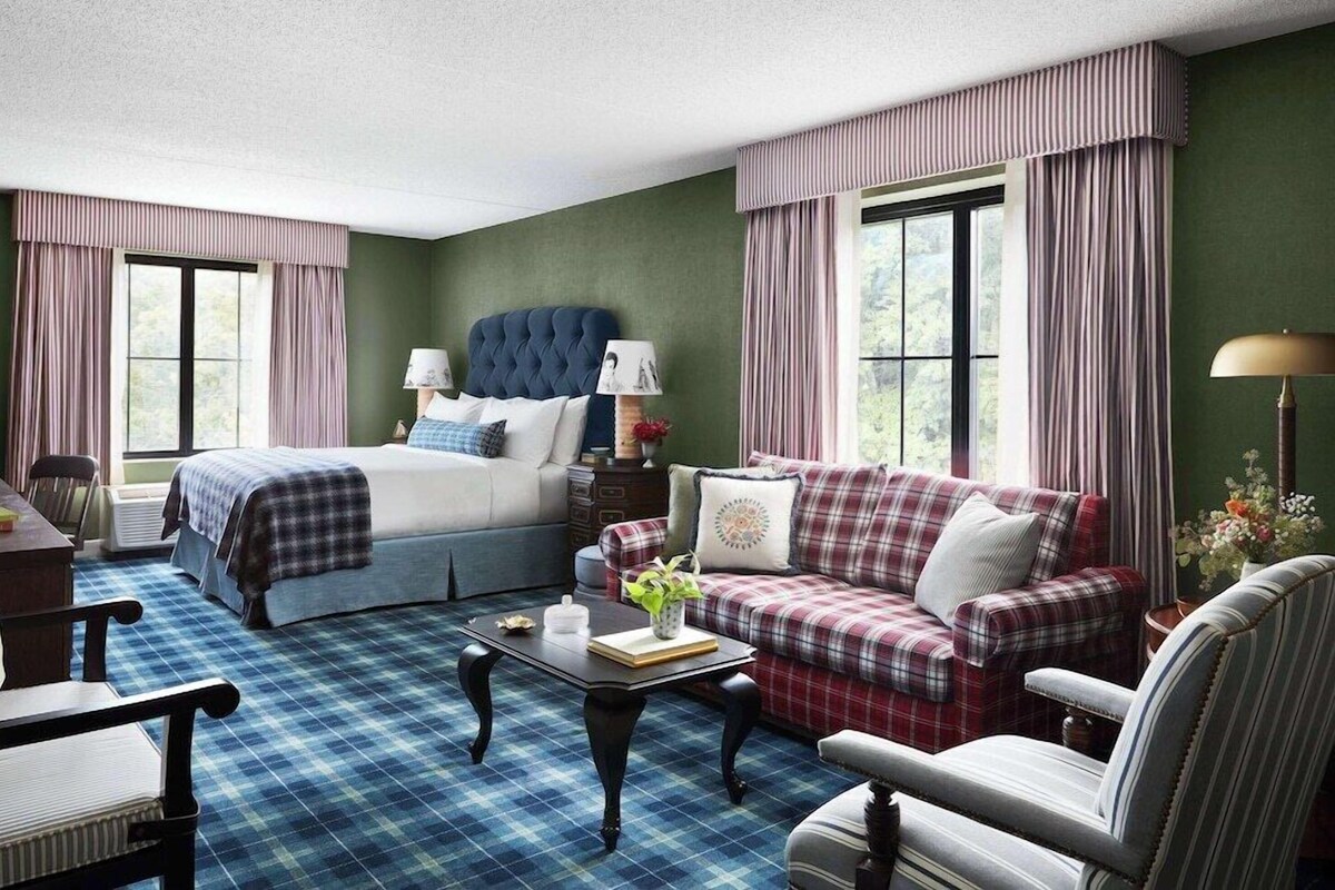 A room with a bed, a sofa, a chair, a table, and a lamp.