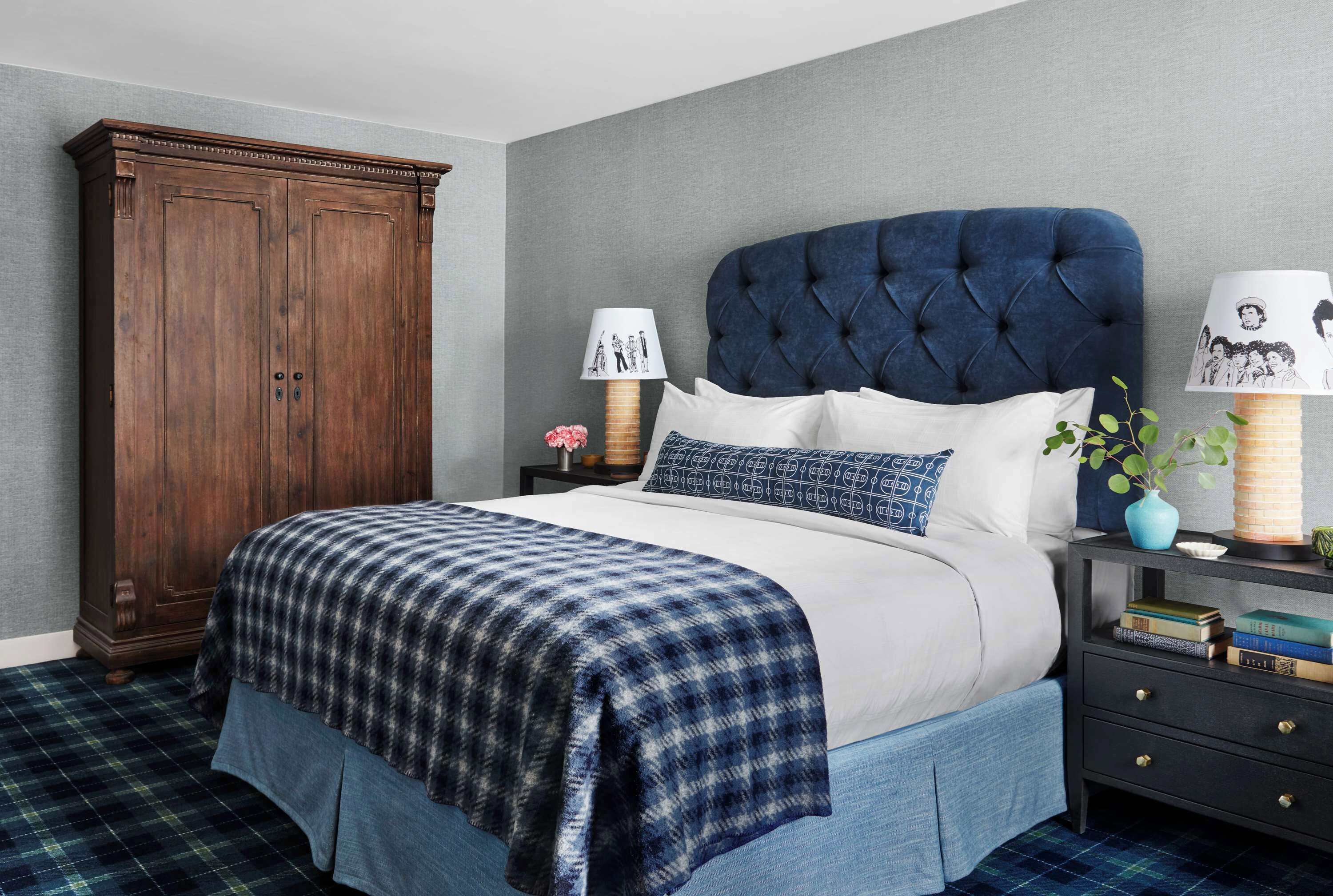 Une chambre avec un grand lit, une armoire en bois sombre, une table de chevet avec des livres et une couvre-lit à carreaux bleus et blancs.