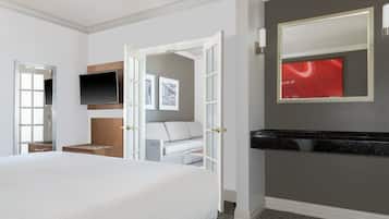 Quarto de hotel com cama, televisão, área de estar com sofá e banheiro com espelho e pia.