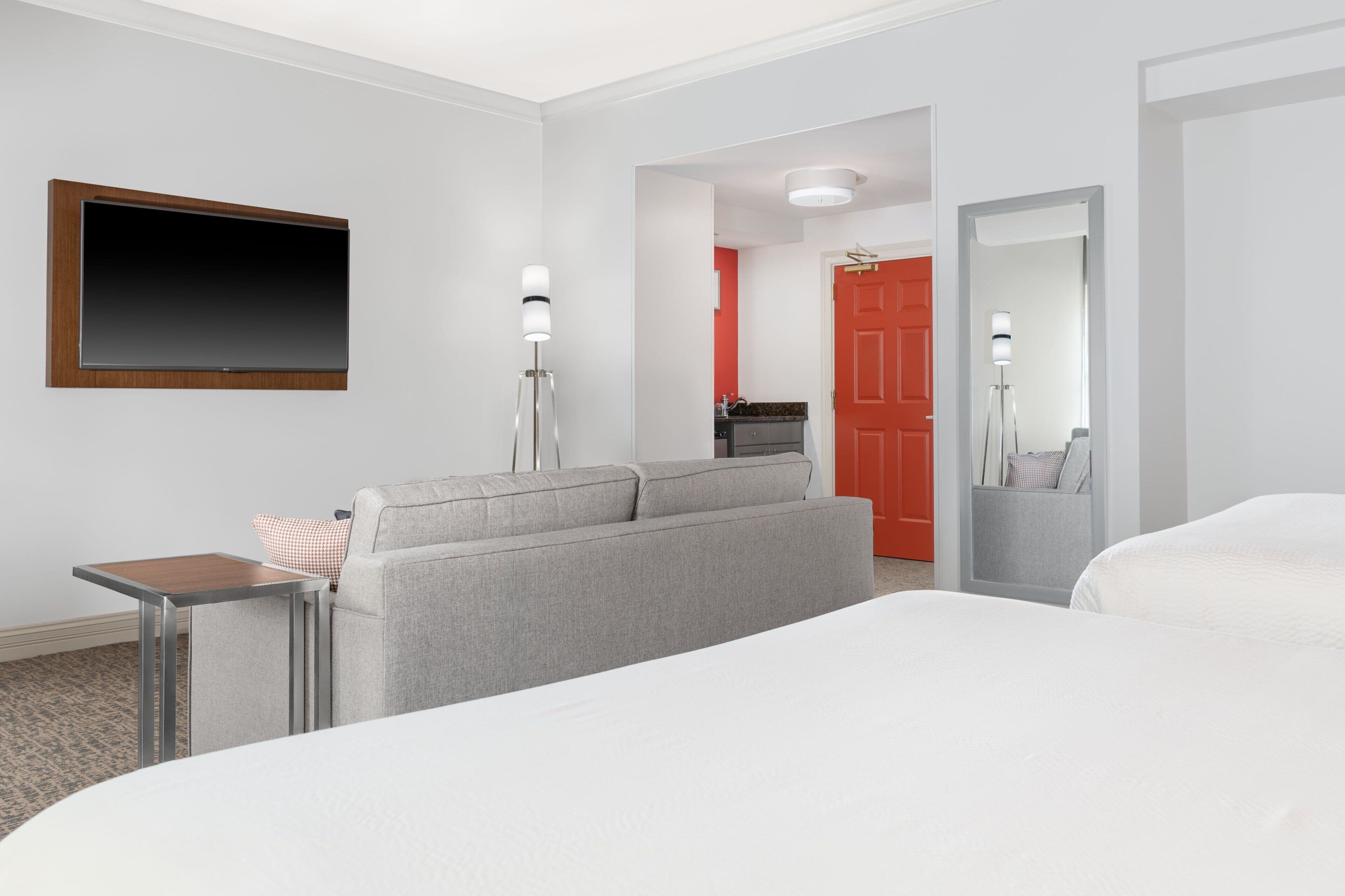 Ein Hotelzimmer mit einem großen Bett, einer Couch, einem Fernseher, einem kleinen Tisch und einem Spiegel.