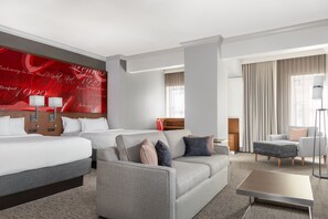 A hotel room with a large bed, a sofa, a coffee table, and a TV. There is a red wall with text and a window with curtains. - Courtyard by Marriott St. Louis Downtown/Convention Center (St. Louis)