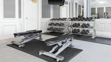 Ein Fitnessstudio mit Hantelbänken, Kurzhanteln und einem Fernseher.