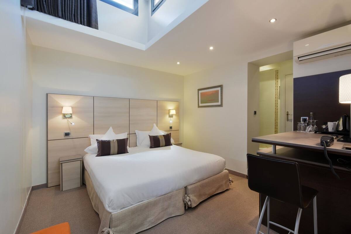 A hotel room with a bed, bedside tables, a desk with a chair, a mirror, and a picture on the wall.
