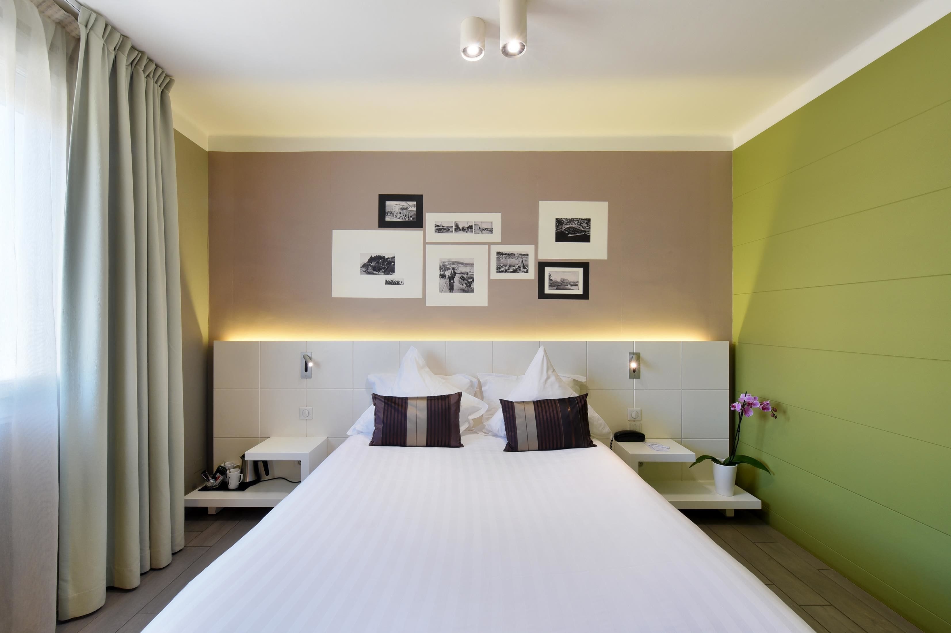 A hotel room with a large bed, two bedside tables, a nightstand, a wall-mounted light, and a green accent wall.