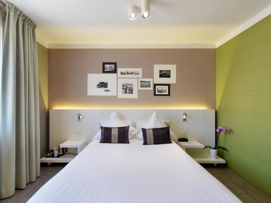 A hotel room with a large bed, two bedside tables, a nightstand, a wall-mounted light, and a green accent wall.