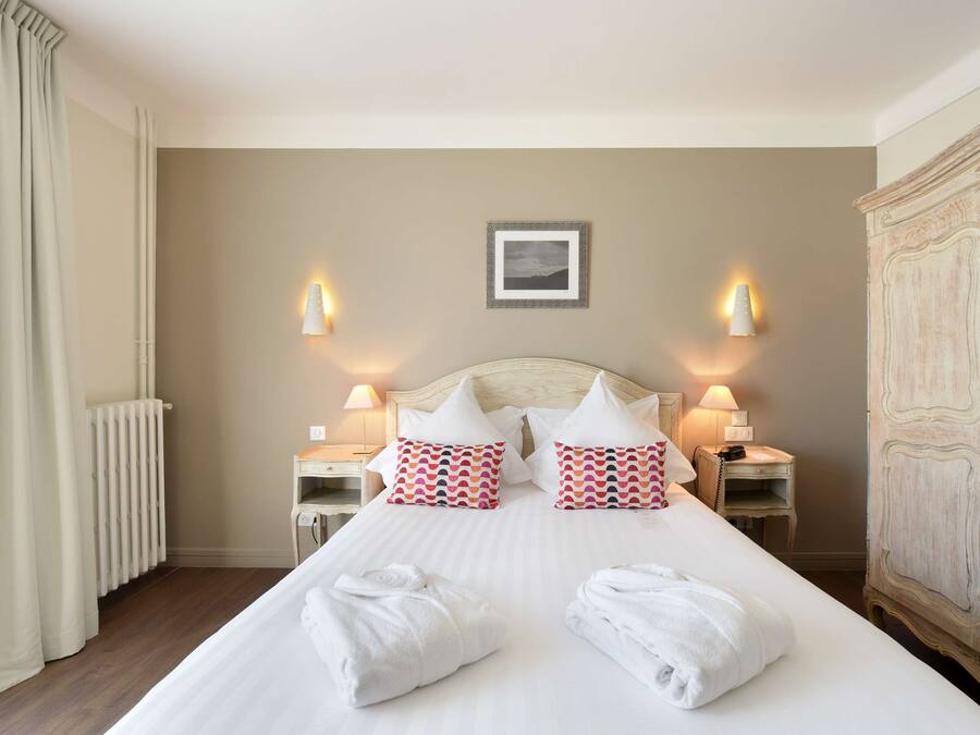 A hotel room with a large bed, two bedside tables with lamps, a radiator, and a wardrobe.