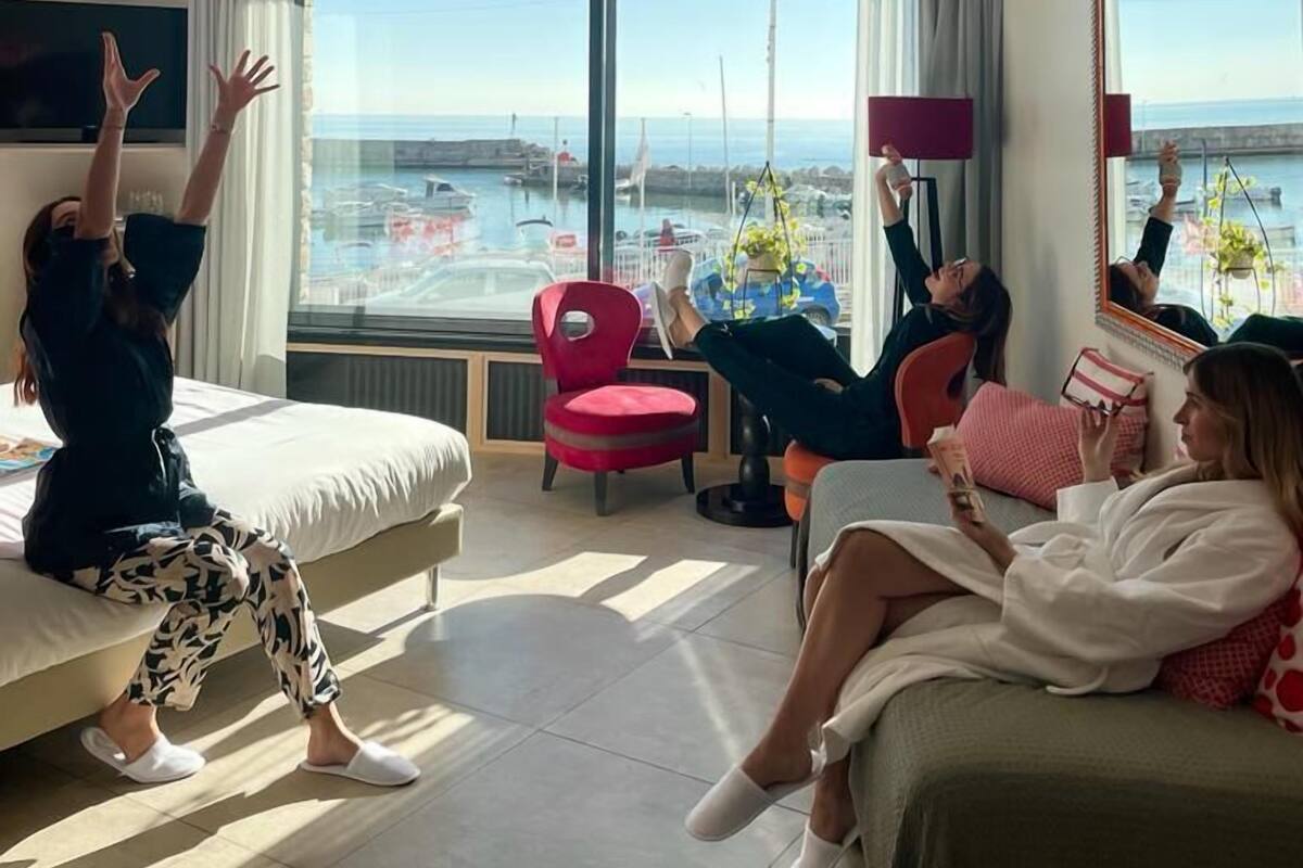 A modern hotel room with a large bed, a red chair, and a view of the marina through large windows.