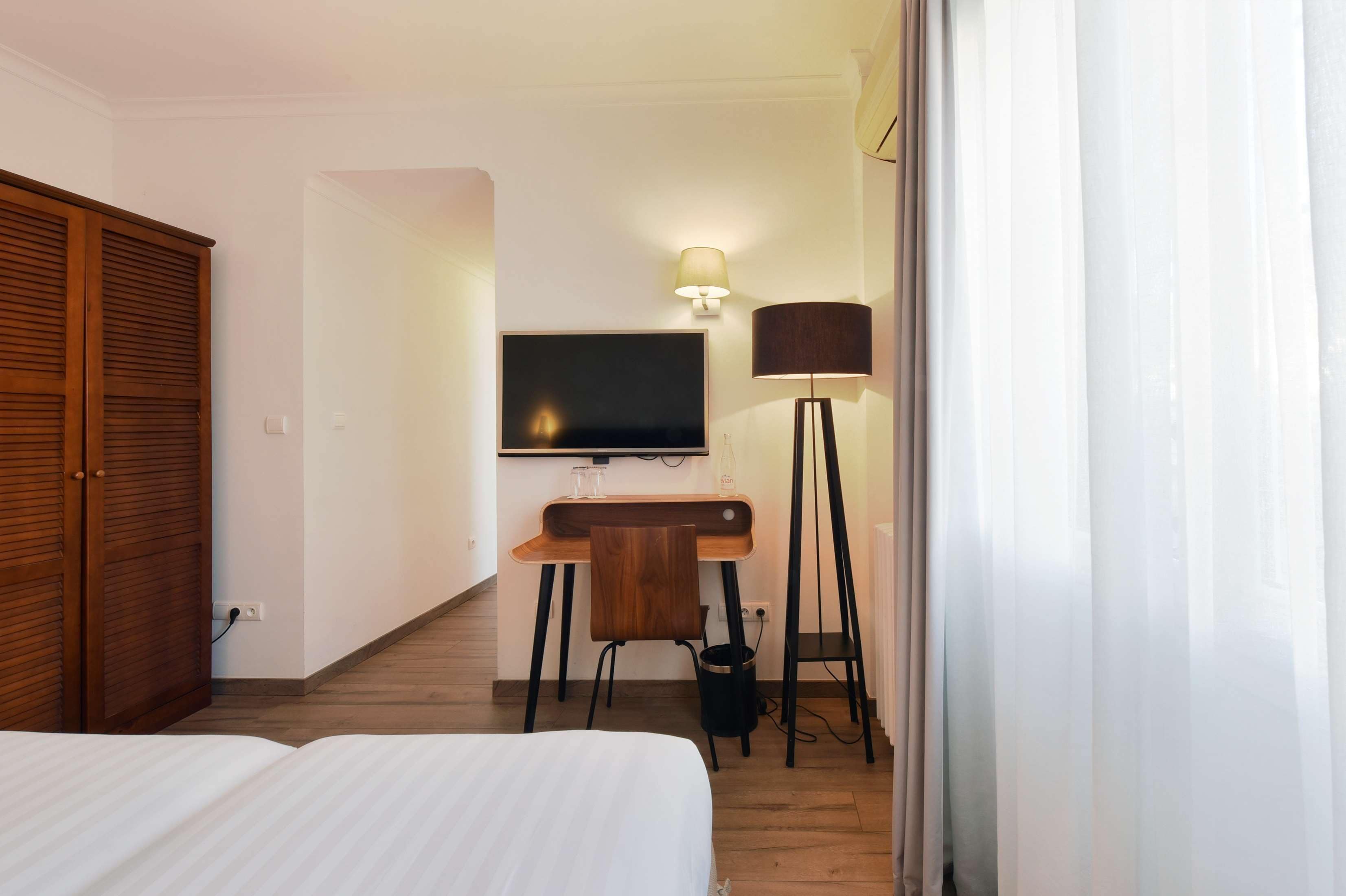 Ein Hotelzimmer mit Bett, Schreibtisch mit Stuhl, Fernseher, Lampe und Kleiderschrank.