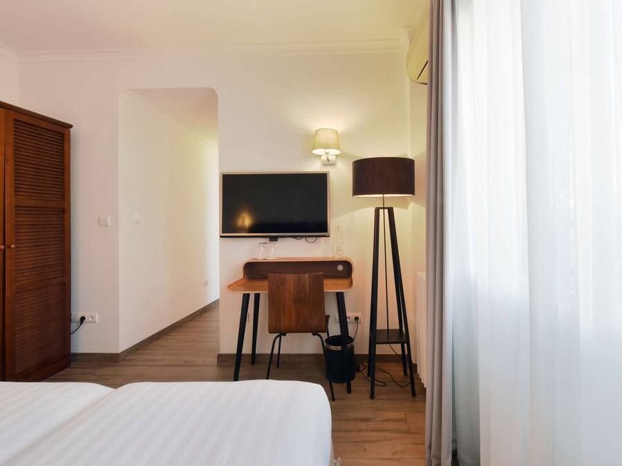 Ein Hotelzimmer mit Bett, Schreibtisch mit Stuhl, Fernseher, Lampe und Kleiderschrank.