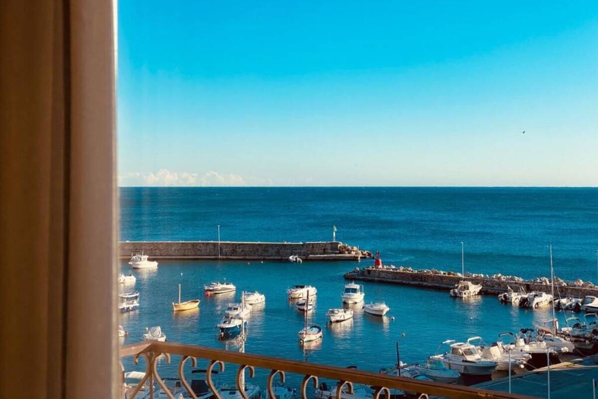 A marina with multiple boats docked, a clear blue sky, and a distant cityscape.