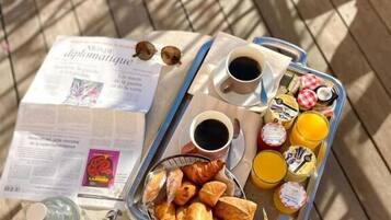 A breakfast tray with croissants, juice, and coffee on a wooden table with a newspaper.