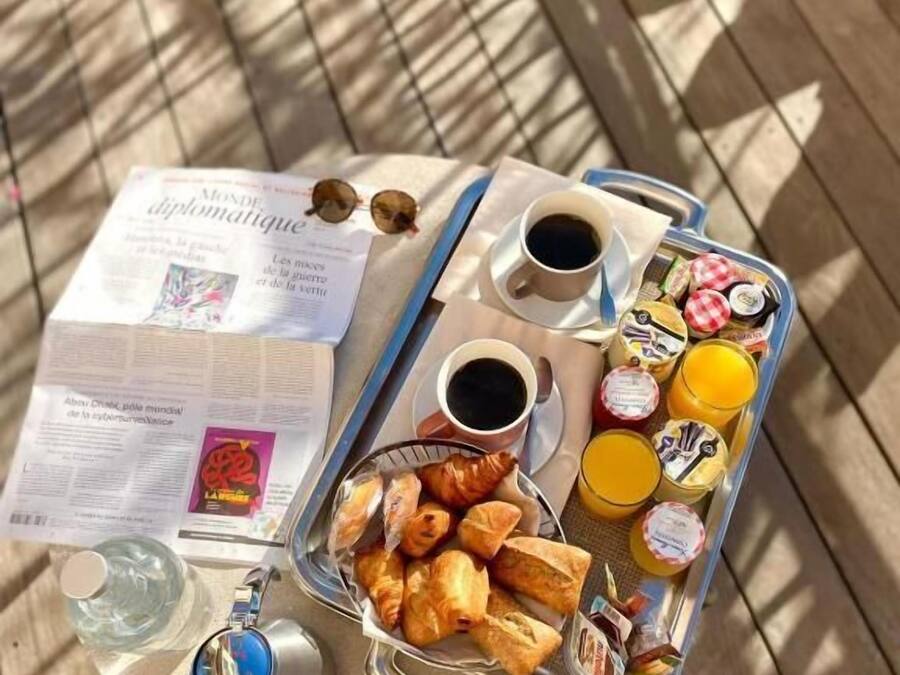 A breakfast tray with croissants, juice, and coffee on a wooden table with a newspaper.