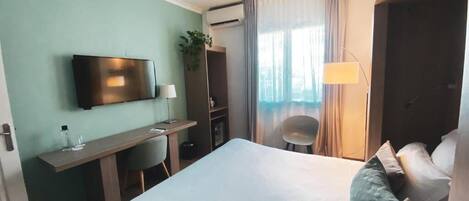 Una habitación de hotel con cama, escritorio, televisor, silla y lámpara.