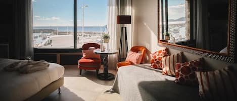 Habitación de hotel con una cama grande, un sofá, una mesita y vistas al mar y al paisaje urbano.