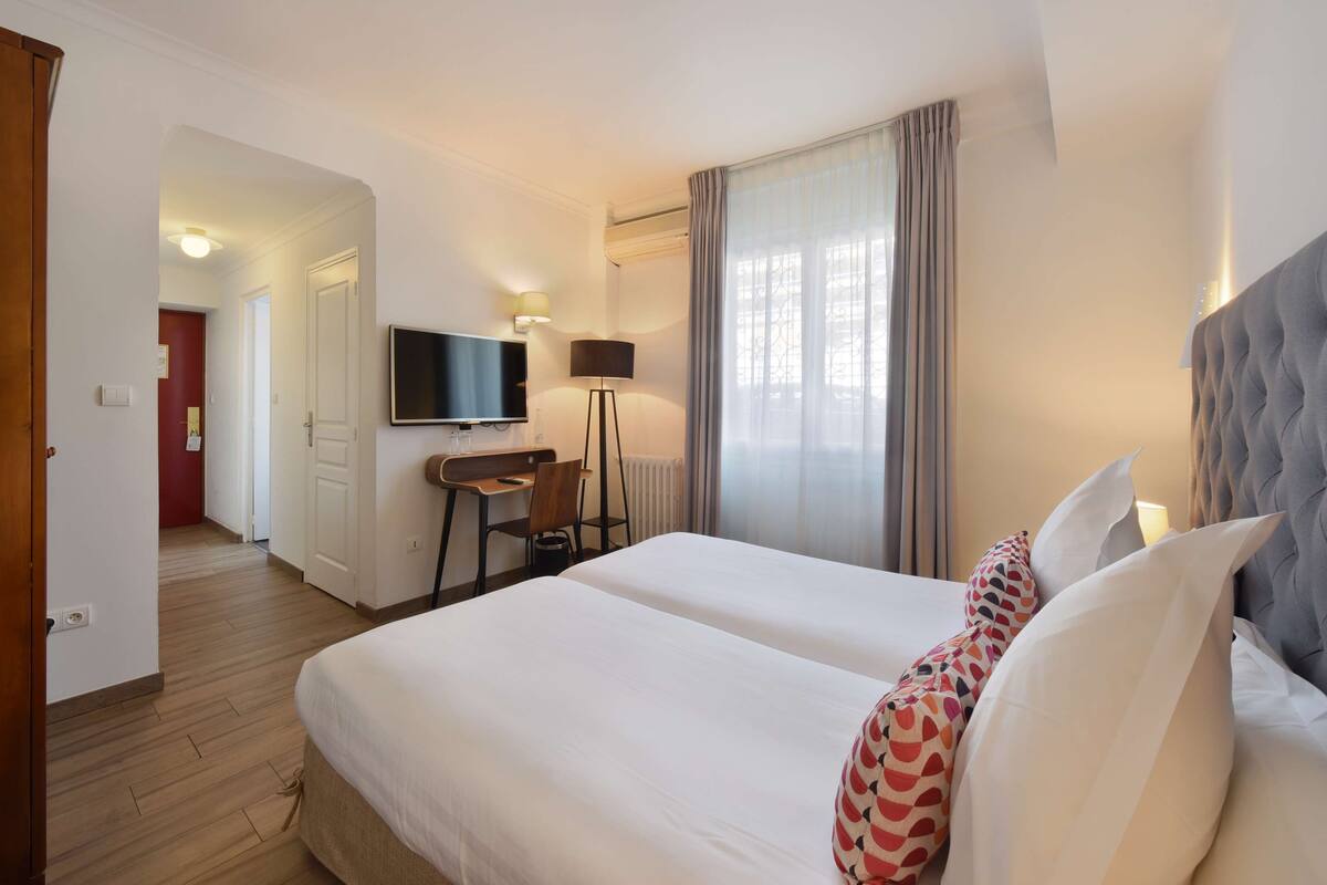A hotel room with a bed, a desk, a chair, a TV, and a window with curtains.