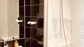 A modern bathroom with a glass-enclosed shower, a white sink, and black tiled walls.