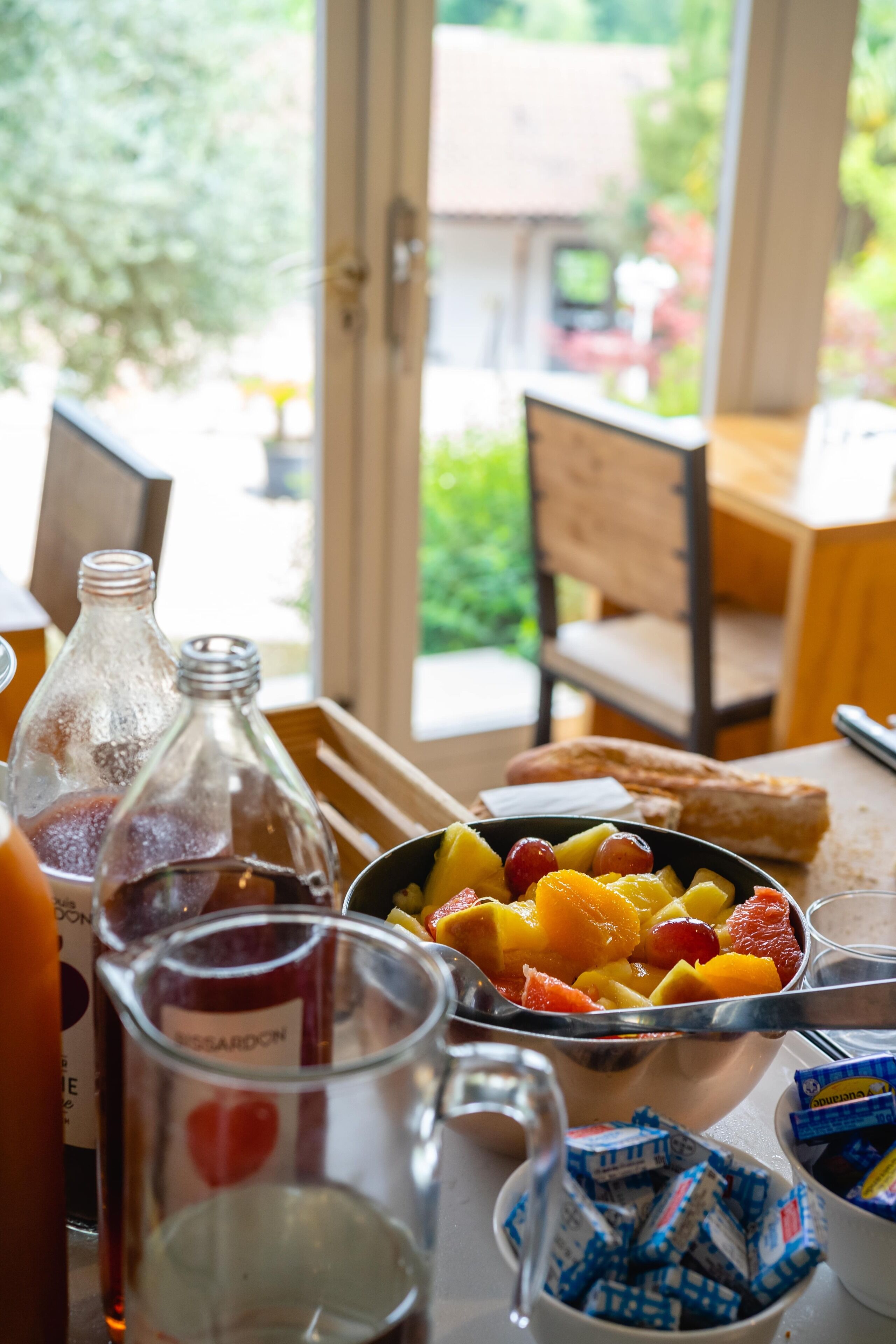 Una mesa de comedor con un frutero, una botella y una jarra de vidrio.