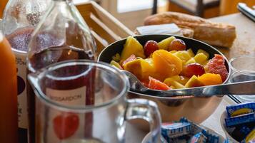 Una mesa de comedor con un frutero, una botella y una jarra de vidrio.